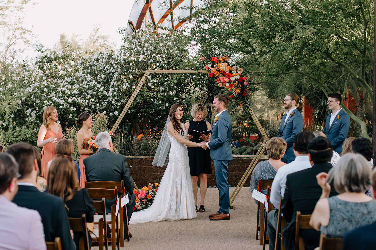 Hands held through the vows under a hexagon arch, with everyone they love packed into the rows on either side.